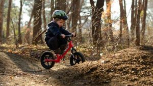 Small child on a Strider bike wearing a helmet and riding on a mountain bike trail