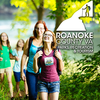 Pre-teen girl wearing glasses, a purple graphic tee, and a backpack on a hike, followed by an adult women with red hair, a backpack, and a blue shirt. There are two young girls hiking behind them.