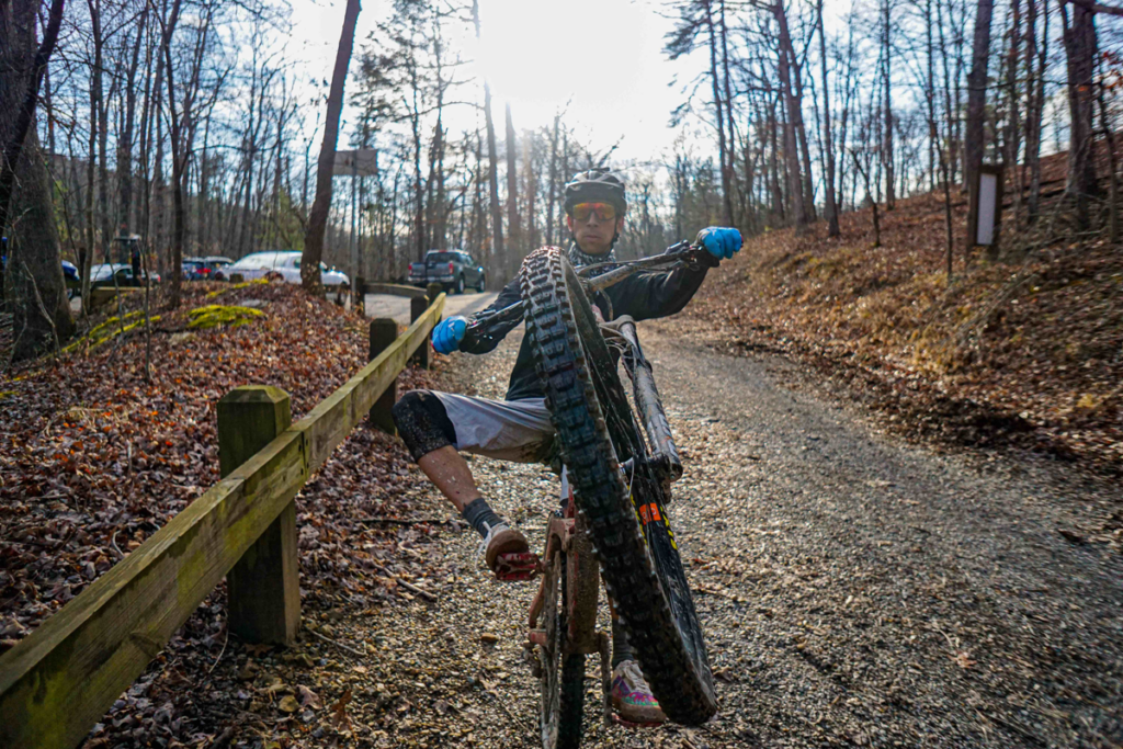 On a winter day, a mountain biker does wheelie on gravel road.