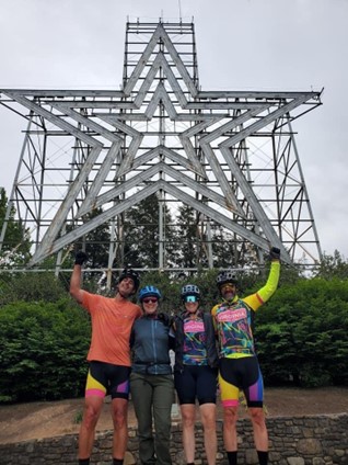 Four cyclists in cycling gear pose under the Roanoke Star.