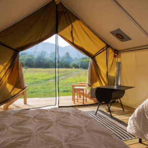 Inside a large, luxury tent facing toward a beautiful, green field and blue mountains.