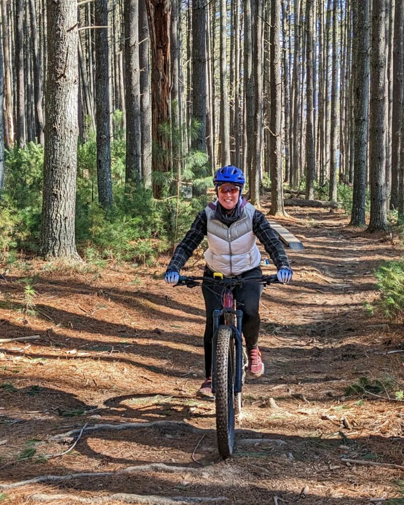 Woman smiles at the camera as she mountain biking through a dense forest in Southwest Virginia.